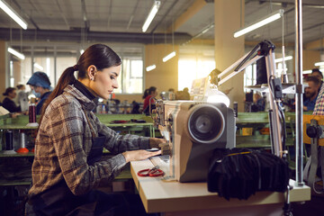 Shoe or clothing factory worker at work. Serious woman working at table with industrial sewing machine in workshop room, side view profile portrait. Footwear and clothes manufacturing industry concept