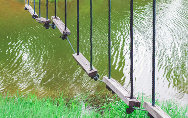 Many swings made of wooden board and tied with rope hang on cable over a small stream flowing through a tropical green rainforest. Swing hanging high and frightening above the river. Selective focus.