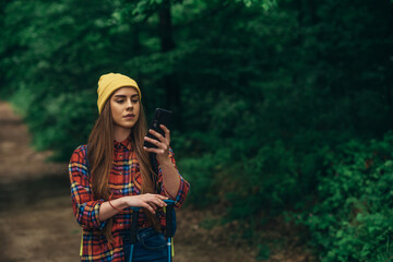 A hiker woman walking in the forest using trekking poles and smartphone