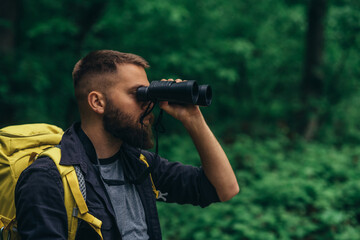 Fototapeta na wymiar A hiker man walking in the forest using binocular and wearing backpack