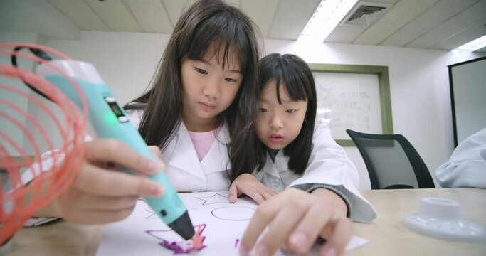 Group of joyful asian elementary students using 3d drawing tool melted plastic is extruded out of the pen on the paper in the classroom. Science and education.