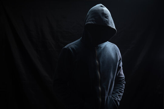 a man in a hood stands on a black background