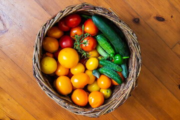 ripe juicy tasty natural red and yellow tomatoes and green cucumbers in a wicker basket, healthy food concept