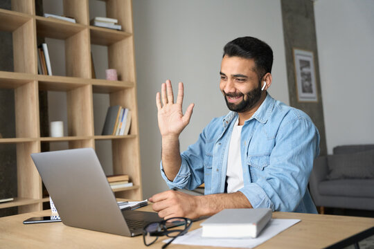 Young Happy Indian Arab Eastern Man Talking On Video Conference Call Greeting Waving Hand Using Laptop At Modern Home Office. Remote Distant Online Communication Technologies Concept.