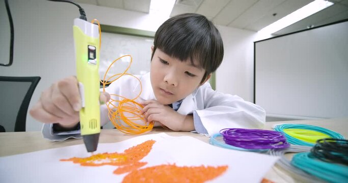 Happy little boy using 3d drawing tool melted plastic is extruded out of the pen on the paper in the classroom. Science and education.
