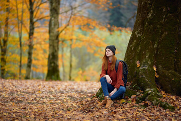 portrait of a woman in a sweater and jeans and a hat under a tree in the autumn forest