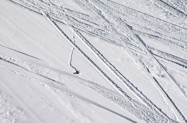 Groomed snowy ski slope with trace from skis, snowboards and stone at winter