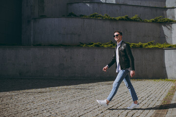 Young full length side view fun smiling happy tourist man 20s wear leather jacket glasses walking...
