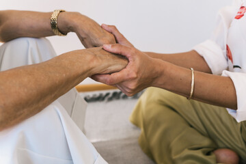 Close up view of senior and young woman holding hands while sitting at home.