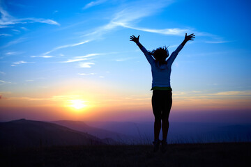 Fototapeta na wymiar Silhouette of happy jumping woman in mountains at sunset