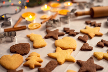 Gingerbread in different shapes on the table with burning candles on the background. Homemade cookies made of white and dark chocolate dough on the table