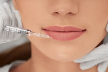 Close up of beautician in white rubber gloves holding syringe and doing injection lip augmentation. Concept of beauty procedure with special preparatus in professional beauty salon. 