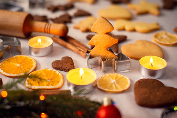 Concept of Christmas baking. Baked cookie in the shape of a christmas tree on the table with burning candles and other decorations around