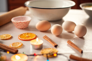 Preparations for baking christmas cakes, bread or cookies. Eggs, rolling pin, slices of dried orange, cinnamon, burning candles and a big empty bowl on the table