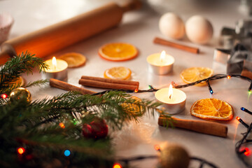 Obraz na płótnie Canvas Christmas baking table. Decorated table with branches of christmas tree, garland, cinnamon sticks, slices of orange, candles. Rolling pin, some eggs on the background
