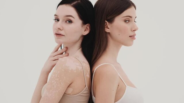 The two girls standing back to back and turning to the camera in a white studio