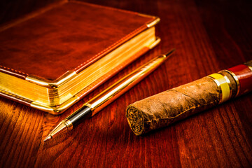 Golden pen with a leather diary and cuban cigar on a mahogany table