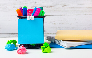 Against a light background of a wooden wall, there is a stand with multi-colored felt-tip pens,...