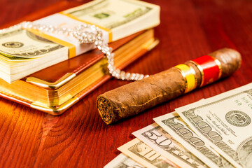 Money with a leather diary and cuban cigar with jewellery on a mahogany table