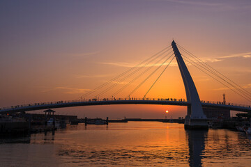 Obraz premium The dock under the dreamy sunset and many tourists walking on the cable-stayed bridge form a beautiful silhouette