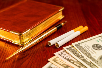 Money with a leather diary and cigarettes with golden pen on a mahogany table