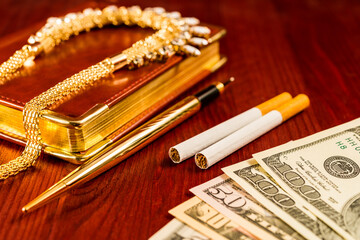 Money with a leather diary and cigarettes with golden chain on a mahogany table