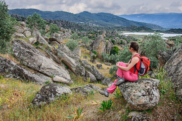 Naklejka na ściany i meble Girl with a backpack on her back resting on a stone looking at a valley in turkey