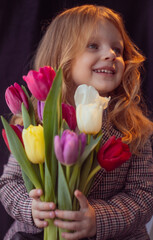 Obraz na płótnie Canvas little girl with flowers tulips on a dark background