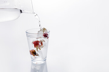 Glass of water with frozen roses in ice cubes on white background