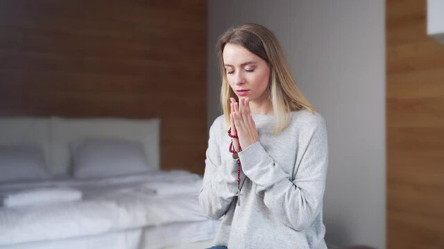 portrait young girl or woman sincerely praying on rosary at home. Prayer of repentance. Female believer with closed eyes and a beads in his hands. Christian or Orthodox Catholic in daily prayers