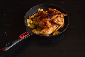 Chicken baked in a pan with potatoes, on a dark wooden background.