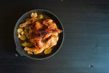 Chicken baked in a pan with potatoes, on a dark wooden background.
