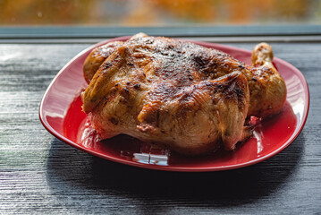 Delicious baked chicken on a red plate, on a wooden background.