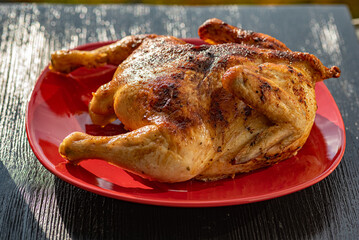 Delicious baked chicken on a red plate, on a wooden background.