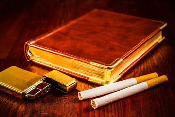Leather diary and cigarettes with open golden lighter on a mahogany table