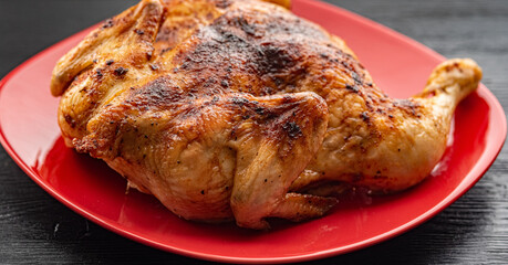 Delicious baked chicken on a red plate, on a wooden background.