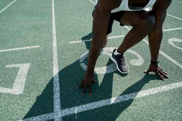 Close up. An African American male athlete prepares for a race on a surface with markings at a sports stadium. Outdoor exercise. Healthy lifestyle concept