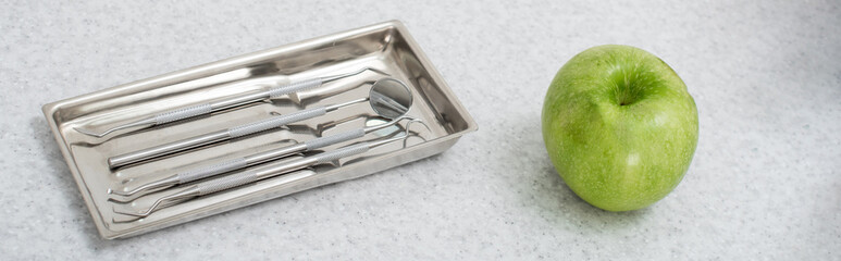 high angle view of metal dental tools in tray and green apple on medical table, banner.