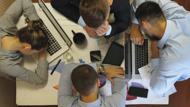 Young exhausted managers napping on table at office. Displeased male boss awaking and waking up his employees to continue working with papers. Sleepy colleagues stretching and rubbing eyes. Top view