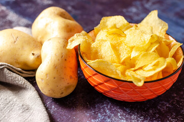 Still life of a bowl of potato chips with raw potatoes and a linen cloth.