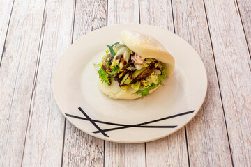 White plate with Asian duck loin bao bread with green sprout salad