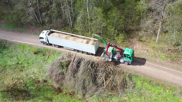 Aerial view of wood chipper blowing shredded wood into back of a truck. Forest background