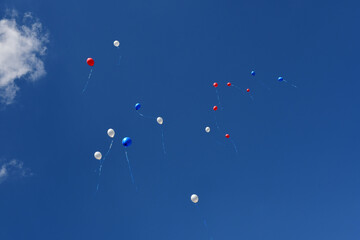 White, blue and red balloons fly away into the clear blue sky.
