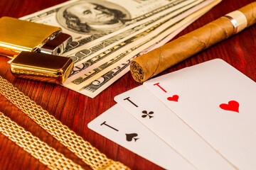 Cuban cigar and golden chain with playing cards and money on the table mahogany. Focus on the cuban...