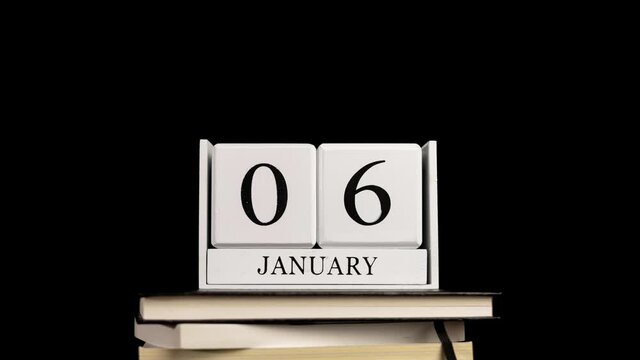 Cube wooden calendar on a pile of books, on every first day of months, hand sets on the calendar with black background.