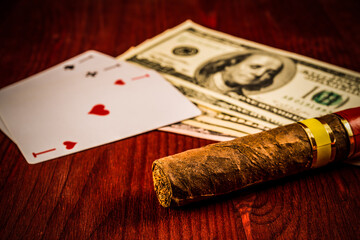 Cuban cigar with playing cards and money on the table mahogany. Focus on the cuban cigar,...