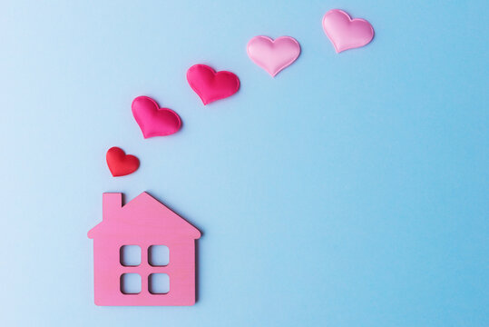 Pink toy house and decorative hearts on light blue background with copy space