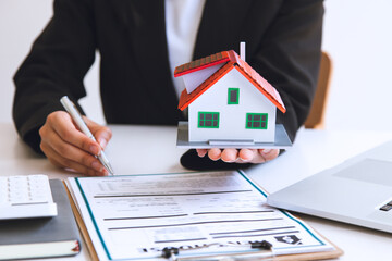 The businessman discusses the terms of the home purchase contract and asks the customer to sign a...
