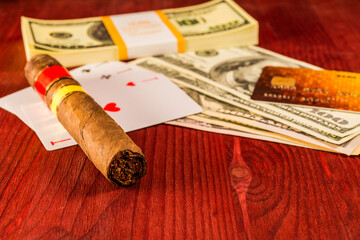 Fototapeta na wymiar Cuban cigar with playing cards and money with payment card on the table mahogany. Focus on the cuban cigar, identification cards ace Russian letter