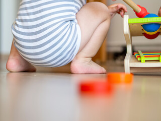 Baby boy crouched or sitting on the floor while playing with colorful toys and discovering....